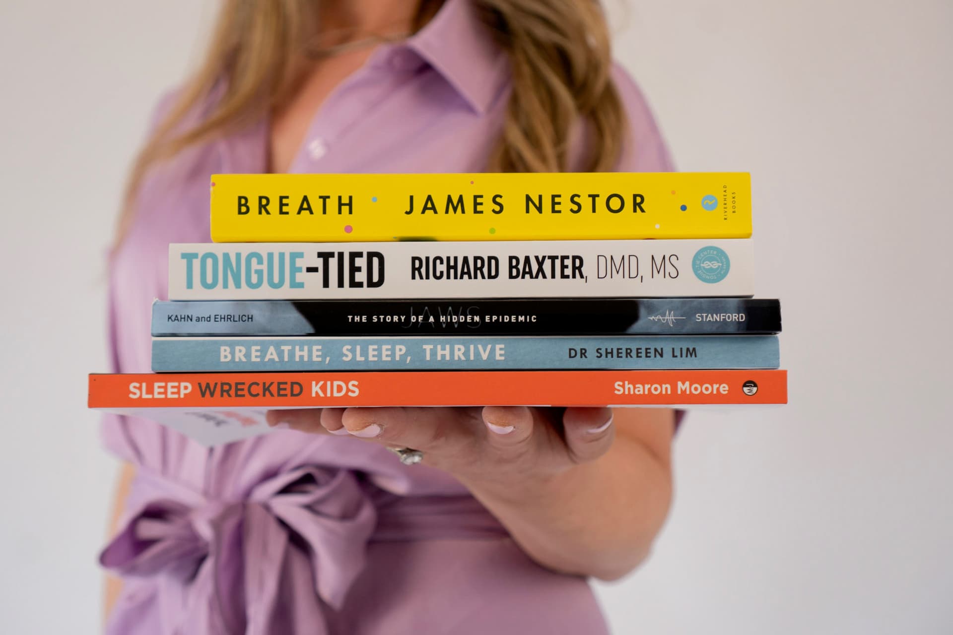 Laura Friedman holding myofunctional and breathing-disorders reference books — Breath by James Nestor, Tongue-Tied by Richard Baxter, Jaws by Kahn and Ehrlich, Breathe Sleep Thrive by Dr Shereen Lim, Sleep Wrecked Kids by Sharon Moore